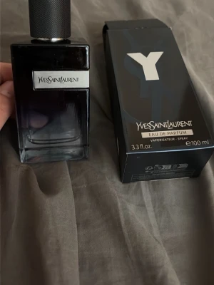 Yves Saint Laurent Y Eau de Parfum - Yves Saint Laurent Y Eau de Parfum i en elegant mörkblå glasflaska med silverdetaljer och svart texturerad kork. Flaskan har en stilren design och medföljande originalkartong. Volymen är 100 ml. Hellt ny