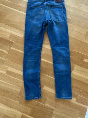Blå slim fit jeans - Säljer ett par blå slim fit jeans med klassisk femficksdesign och snygga slitningar på framsidan. Jeansen har normal midja och raka ben. Perfekta till en avslappnad stil och passar till det mesta i garderoben.