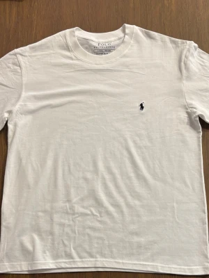 Vit t-shirt från Polo Ralph Lauren - Klassisk vit t-shirt från Polo Ralph Lauren med rund halsringning och korta ärmar. T-shirten har en liten mörkblå broderad logga på bröstet. Start priset 500 kr. 