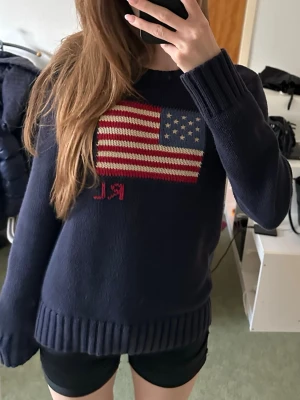 Mörkblå stickad tröja Ralph Lauren - Mörkblå stickad tröja från Ralph Lauren med amerikansk flagga och RL-broderi. Tröjan har rund hals, långa ärmar och breda ribbade muddar vid ärmslut och nederkant. Den är storlek L i barn (14-16 år) och passar mig som bär Xs-S. Nypris: 2395kr. 🩷