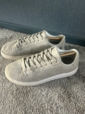 Sommar skor - Snygga ljusgrå sneakers med stilren design och matchande snörning. Skorna har en låg siluett och ovandel i mockaliknande material samt vit sula. Perfekta för dig som gillar en clean och enkel look.