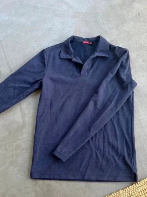 Mörkblå långärmad Piké  - Snygg mörkblå långärmad tröja från RYVLS med klassisk krage och utan knappar. Tröjan har en enkel och clean look, perfekt att bära över en skjorta. Pris kan diskuteras!