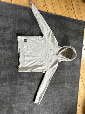 Morris hoodie - Ljusgrå hoodie från Morris med liten broderad logga på bröstet och patch vid nederkanten. Klassisk passform, långärmad och med huva samt dragsko. Perfekt för en avslappnad och cool look.