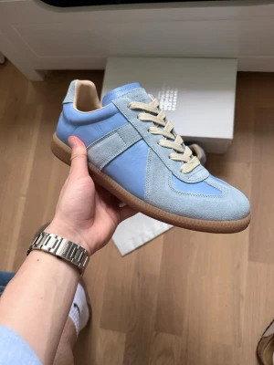 Maison margiela gats - Snygga sneakers från Maison Margiela i ljusblått läder och mocka med beige detaljer och gummisula. Klassisk low-top siluett med beige snören och stilren design som passar till många outfits.