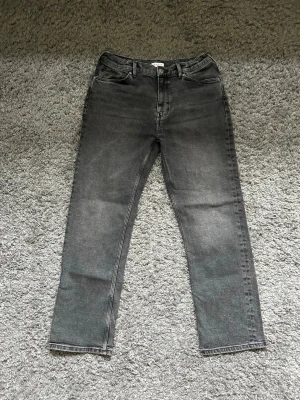Gant Grå raka jeans med hög midja - Säljer ett par Gant grå jeans med rak passform och hög midja. Jeansen har klassiska fem fickor, bälteshällor och dragkedjegylf. Materialet är denim i bomull och färgen är tvättad grå för en cool vintage-look.