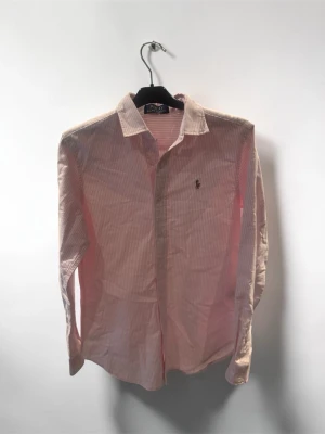 Rosa randig skjorta från Polo Ralph Lauren - Säljer en klassisk rosa och vit randig skjorta från Polo Ralph Lauren. Riktigt fin sommarskjorta som passar bra till allt Storlek M och passar dig runt 175-180. Säljes då den var förliten och inte gick att returnera då jag råkade tappa bort följesedeln