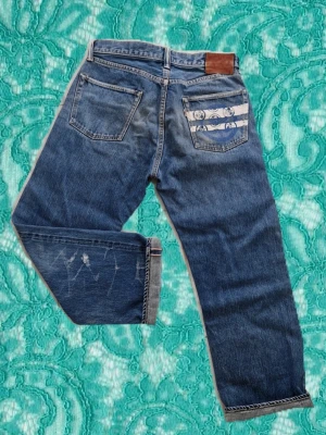 Momotaro Jeans (Very rare) - Ett par riktigt unika och sällsynta jeans av Momotaro som är gjorda i Japan av högkvalikativt Selvedge i storlek W30. Jeansen har den legendariska sashiko loggan på bakfickan som sammanatrålar hela Momotaros japanska historia. Mått: Midja: 39cm Benlängd: 90cm Innerbenslängd: 64cm Benbredd vid slutet: 19cm