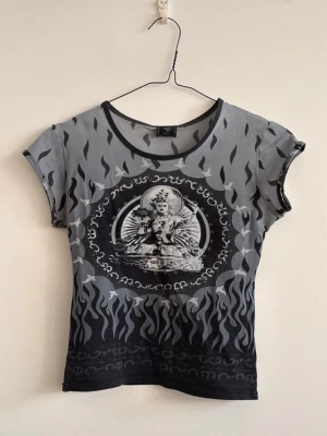 Grå och svart t-shirt med tryck - Unik t-shirt från Free Paris i grått och svart med grafiskt tryck framtill och eldliknande mönster. T-shirten har korta ärmar och rund halsringning. Perfekt för dig som gillar alternativ stil och detaljerade motiv.