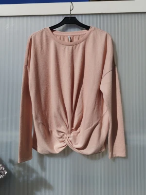 Ljusrosa långärmad topp från ONLY - Trendig ljusrosa långärmad topp från ONLY med rund halsringning och snygg twistad knutdetalj framtill. Tillverkad i mjukt material som känns skönt mot huden. Perfekt för dig som gillar en enkel men ändå unik look. Lite nopprig men annars fint skick.