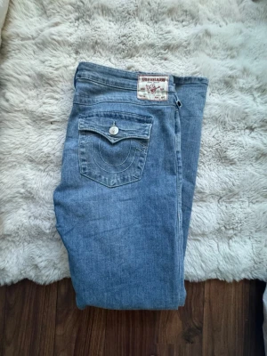 True Religion Joey flare jeans blå - Säljer ett par blå Joey Low Rise Flare jeans från True Religion. Klassisk femficksmodell med snygga kontrastsömmar och ikonisk fickdetalj bak. Tillverkade i mjuk denim med låg midja och utsvängda ben. Perfekta för en avslappnad men trendig look. Fint skick och inga konstigheter. Hör av er vid frågor och pris kan diskuteras.💕
