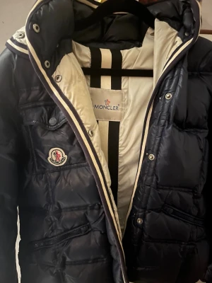 Mörkblå dunjacka från Moncler - Snygg mörkblå dunjacka från Moncler med vit insida och klassisk logga på bröstet.  Perfekt till vintern då jag använde denna i mer än 26 minus å inte frös alls, medans jag slippte gå runt med en stor jacka som andra.