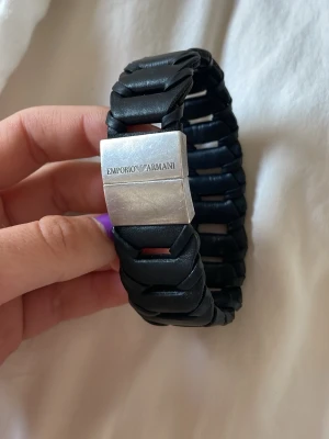  Emporio Armani silver/ läder Svart flätat armband - Snyggt svart flätat armband från Emporio Armani med bred design och silver spänne där loggan är ingraverad. Armbandet är gjort i läder och har en modern, stilren look som passar perfekt till din outfit. Riktigt läder och silver ( 925)