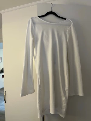Vit långärmad klänning med snörning - Säljer en stilren vit klänning med lång ärm och snörning vid halsen. Klänningen har en enkel, rak form och är tillverkad i ett mjukt material som ger en skön passform. Perfekt för dig som gillar minimalistisk design och vill ha något klassiskt i garderoben.