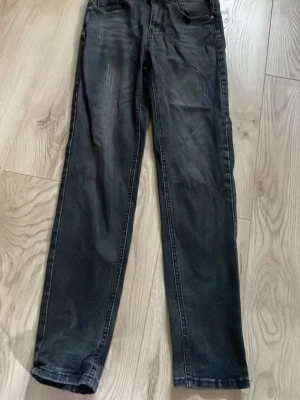 Svarta raka jeans - Säljer ett par svarta jeans med rak passform och klassisk femficksdesign. Jeansen har diskreta slitningar framtill och är tillverkade i ett mjukt denimtyg. Perfekta för en avslappnad och stilren look.