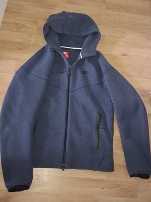 Mörkblå Nike hoodie med dragkedja - Snygg mörkblå hoodie från Nike med hel dragkedja framtill och två fickor med dragkedja. Klassisk huva och diskret Nike-logga på bröstet. Tillverkad i mjukt och bekvämt material, perfekt för en avslappnad stil.