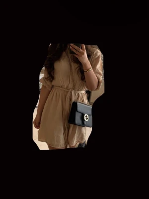 Beige kort klänning från chiquelle - Snygg beige kort klänning från chiquelle med knappar framtill och knytskärp i midjan. Lätt och mjukt material, långa ärmar och avslappnad passform. Perfekt för en trendig och bekväm look speciellt nu till sommaren!🩷OBS: FRAKTAR INOM 24H!🩷
