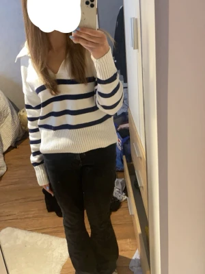 Vit stickad tröja med marinblå ränder - Säljer en vit ”stickad” tröja med marinblå horisontella ränder och v-ringning. Tröjan har en bred krage och långa ärmar med ribbade muddar. Perfekt för en avslappnad och trendig look.
