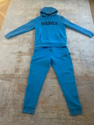 Blå Hoodrich Set - Säljer en Hoodrich set som tyvärr inte kommer till användning längre. Setet är endast använt ett fåtal gånger och är i mycket fint skick, i princip som nytt.  Tröjan är i storlek M och byxorna i storlek L.  Pris kan diskuteras vid snabb och smidig affär. Hör gärna av dig vid intresse eller om du har några frågor!