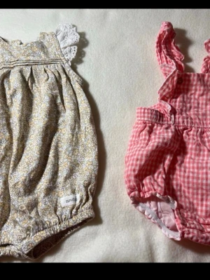 Två söta babyrompers, H&M & Newbie - Två gulliga babyrompers, en från H&M i rosa och vitt rutigt ekologiskt bomullstyg med volangdetaljer, och en från Never i blommigt mönster med spetskant på axlarna. Perfekta för sommaren och riktigt mjuka mot huden.