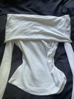 Y2K Vit offshoulder topp  - Trendig vit offshoulder topp från Weekday i mjukt stickat material. Toppen har långa ärmar och en bred kant över axlarna som ger en snygg och modern look. Perfekt att styla med jeans eller kjol för en cool vibe.