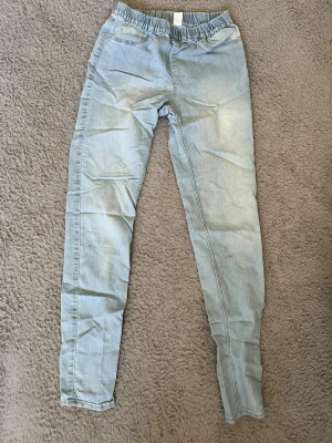 Ljusblå denimleggings med resårmidja - Säljer ett par ljusblå leggings i denimlook med bekväm resår i midjan. De har smal passform och är perfekta för en avslappnad stil. Materialet är stretchigt och mjukt, vilket gör dem sköna att bära hela dagen.