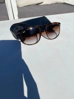 Ray-Ban bruna solglasögon - Snygga solglasögon från Ray-Ban med brunmelerad båge och stora, fyrkantiga glas. Linsfärgen går från mörkbrun upptill till ljusare nedtill. Kommer med original Ray-Ban-fodral.