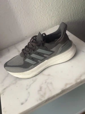 Grå Adidas sneakers med mesh och boost - Snygga grå sneakers från Adidas  ultra boost med klassiska tre ränder på sidan. Ovandelen är i mesh och syntet för bra andningsförmåga och komfort. Sulan är tjock och vit med boost-dämpning för extra skön känsla. Perfekta för dig som gillar sportig stil.