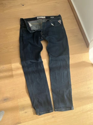 Mörkblå Replay Anbass jeans - Snygga mörkblå jeans från Replay, modell Anbass. Klassisk femficksdesign med raka ben och detaljerade sömmar. Jeansen har en diskret Replay-logga på myntfickan och är tillverkade i slitstarkt denimtyg. Perfekta för en avslappnad och trendig stil.