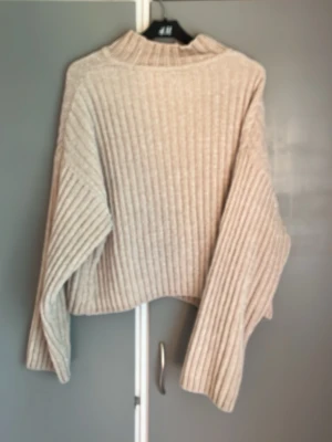 Beige ribbstickad tröja H&M - Säljer en beige ribbstickad tröja från H&M med hög krage och långa ärmar. Tröjan har en avslappnad passform och är gjord i mjukt material, perfekt för kyliga dagar. Enkel och stilren design som passar till det mesta. Storlek L men passar bra till mig som har M!