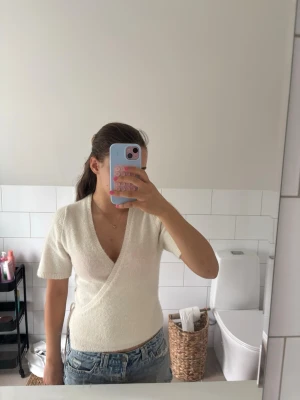Vit omlottopp med kort ärm - Söt vit omlottopp med korta ärmar och djup v-ringning. Toppen har en mjuk, stickad känsla och sitter figurnära. Perfekt att matcha med jeans eller shorts.