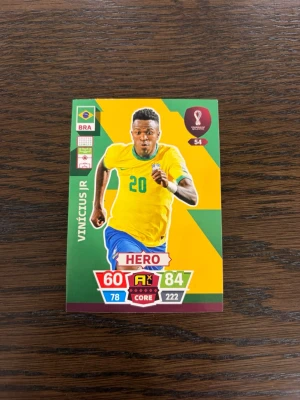 Vini jr fotbollskort HERO - Samlarobjekt: Fotbollskort från FIFA World Cup Qatar 2022. Kortet har färgerna gul, grön och röd med spelare i Brasiliens landslagströja och HERO-klassificering. Nummer 54, med stats och position forward. Perfekt till samlingen!