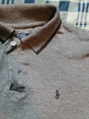 Grå pikétröja från Polo Ralph Lauren - Klassisk grå pikétröja från Polo Ralph Lauren med broderad logga på bröstet. Tröjan har krage, knappar framtill och korta ärmar. Perfekt till en avslappnad men ändå stilren look.