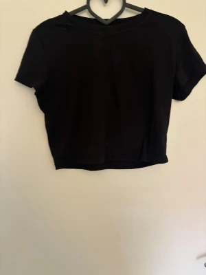 Svart croppad topp - En enkel och stilren svart croppad topp. T-shirten har rund halsringning och korta ärmar. Perfekt att matcha med jeans eller kjol för en trendig look. Finns en likadan fast i vit i min profil
