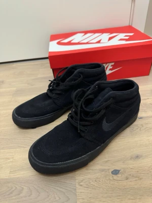 Svarta Nike suede sneakers mids - Säljer ett par helsvarta Nike sneakers i mocka med klassisk swoosh på sidan. Skorna har mellanhögt skaft och svarta skosnören. Snygg och stilren design som passar till det mesta. Kommer med originalkartong.