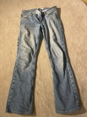 Ljusblå bootcut jeans Junkyard XS - Säljer ett par ljusblå bootcut jeans från Junkyard i storlek XS. Jeansen har klassisk femficksdesign, normalhög midja och är tillverkade i denim. Perfekta för dig som gillar en avslappnad och trendig look.