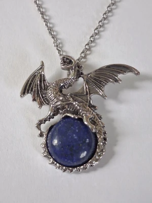 Halsband med drake och blå sten - Unikt halsband med en detaljerad drake i silverfärgad metall som håller en rund, djupblå sten. Kedjan är tunn och matchar hängets metall. Perfekt för dig som gillar fantasy och vill ha ett smycke som sticker ut. Materialet rostfritt stål. 