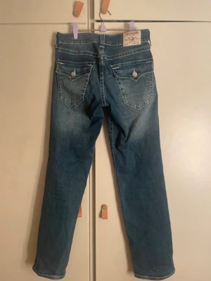 Blå jeans från True Religion - Säljer ett par True Religion jeans i modellen ”Ricky, relaxed straight. De är i storlek W27 och de passar mig som har storlek M. Jag har använt byxorna några gånger men de är i väldigt fint skick!💕 Säljes då de inte kommer till användning längre. 