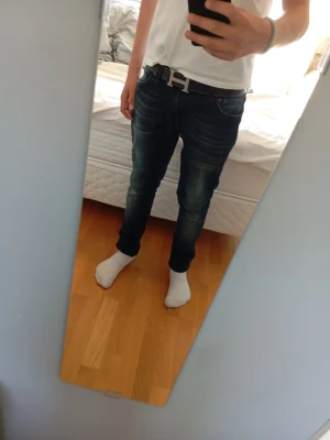 Mörkblå slim fit jeans - Säljer ett par mörkblå slim fit jeans med snygga slitningar och tvättade detaljer. Jeansen har klassisk femficksmodell och sitter tight över benen. Perfekta för dig som gillar en modern och stilren look.