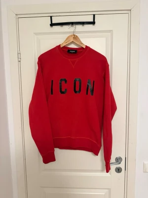 Dsquared2 ICON sweatshirt - Säljer en röd sweatshirt från Dsquared2 med svart 'ICON'-tryck på bröstet. Tröjan har rund hals, långa ärmar och ribbade muddar. Materialet är mjuk bomull som är skönt mot huden. Perfekt för dig som gillar streetwear och vill sticka ut med en ikonisk look. Retail 2500kr, storlek S passar även M.