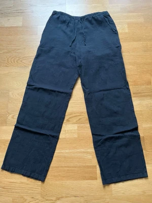 Svarta linnebyxor från Gina young - Snygga svarta linnebyxor från Gina Tricot Young med avslappnad passform och snören i midjan. Tillverkade i luftigt linnematerial som passar perfekt för en chill och stilren look. Byxorna har raka ben och sidofickor. Stl 158/164