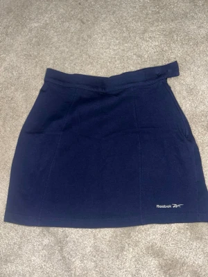 Mörkblå skort från Reebok - Sportig mörkblå skort från Reebok med diskret logga framtill. Klassisk rak passform och bred midjeresår för extra komfort. Tillverkad i mjukt och stretchigt material som passar perfekt för en aktiv stil. Pris kan diskuteras det står M men skulle absolut säga att den är mer åt S 