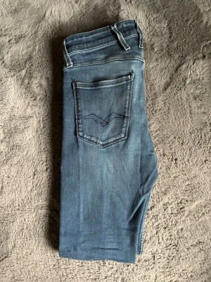 Blå replay anbass jeans - Säljer ett par blå jeans från Replay med klassisk femficksdesign och snygga slitningar. Storlek 28/30. Mycket bra skick inga defekter, knappast använda!