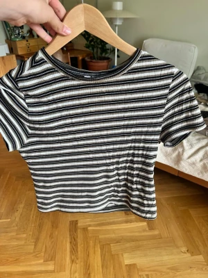 Randig ribbad t-shirt från H&M  - Säljer en ribbad t-shirt från H&M  i svart, vit och grön med horisontella ränder. Modellen är kortärmad och har en tight passform som sitter snyggt. Perfekt till jeans eller kjol för en chill och trendig look.