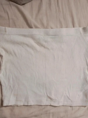 Vit ribbad offshoulder topp - Säljer en enkel och stilren vit ribbad offshoulder topp. Toppen är croppad och har en tight passform som sitter snyggt på kroppen. Perfekt att matcha med höga jeans eller kjol för en trendig look.