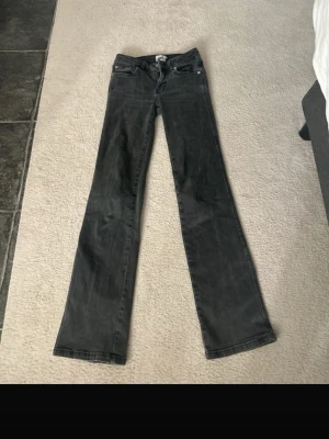 Svarta bootcut jeans med fickdetaljer - Säljer ett par svarta bootcut jeans med klassisk femficksdesign och snygga ficklock med knappar bak. Jeansen har normal midja och raka ben som går ut lite nedtill. Perfekta till en avslappnad streetstyle-look.