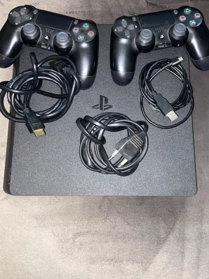 PlayStation 4 Slim med två kontroller - Säljer en svart PlayStation 4 Slim från Sony. Konsolen är stilren och kompakt med matt finish. Två svarta DualShock 4-kontroller och tillhörande kablar (HDMI och USB) ingår. 