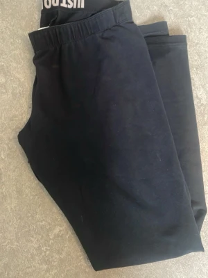 Svarta leggings från Nike - Säljer ett par svarta leggings från Justcool med elastisk midja och smal passform. Tillverkade i mjukt och stretchigt material som sitter skönt på kroppen. Perfekta till både träning och chill. Klassisk och enkel design utan detaljer. Urtvättade och slitna men funkar perfekt för mys eller hundpromenader eller som extra leggings för träningen