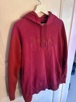Röd hoodie från Tiger of Sweden Jeans - Säljer en snygg röd hoodie från Tiger of Sweden Jeans med broderad logga på bröstet. Hoodien har huva med snörning och långa ärmar. Perfekt för dig som vill ha en stilren men ändå cool look.
