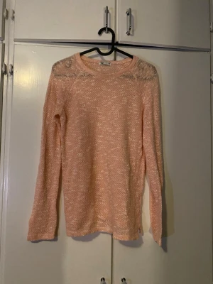 Aprikosfärgad stickad tröja med meshdetalj - Den är lite aprikosfärgad, dåligt ljus❗️ Aprikosfärgad stickad tröja med lång ärm och rund hals. Tröjan har en lätt transparent meshdetalj upptill vid axlarna och är tillverkad i ett mjukt, tunt material. Perfekt för lager på lager och en avslappnad look.