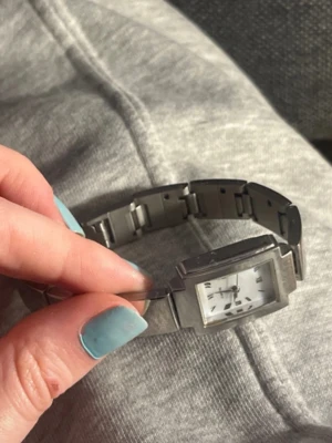 Stilren silverfärgad armbandsklocka - Snygg armbandsklocka i silverfärgat metall med rektangulärt ur och länkarmband. Tydlig vit urtavla med svarta markeringar och visare. Perfekt accessoar för dig som gillar en clean och modern look.